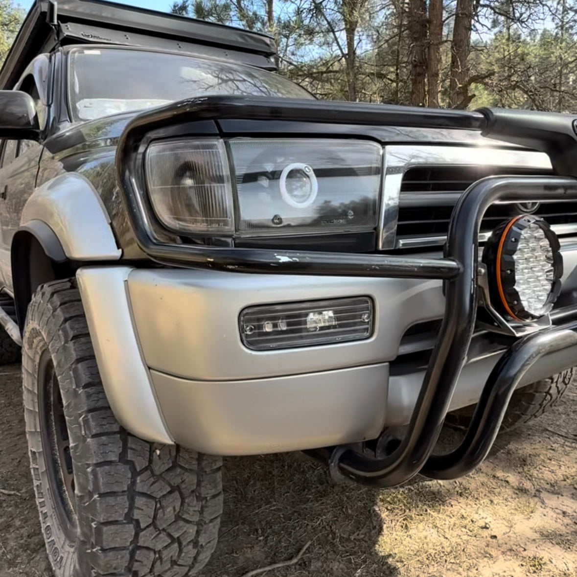 Close-up of a vehicle's front bumper and headlight with a forest background
