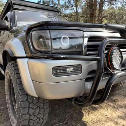Close-up of a vehicle's front bumper and headlight with a forest background