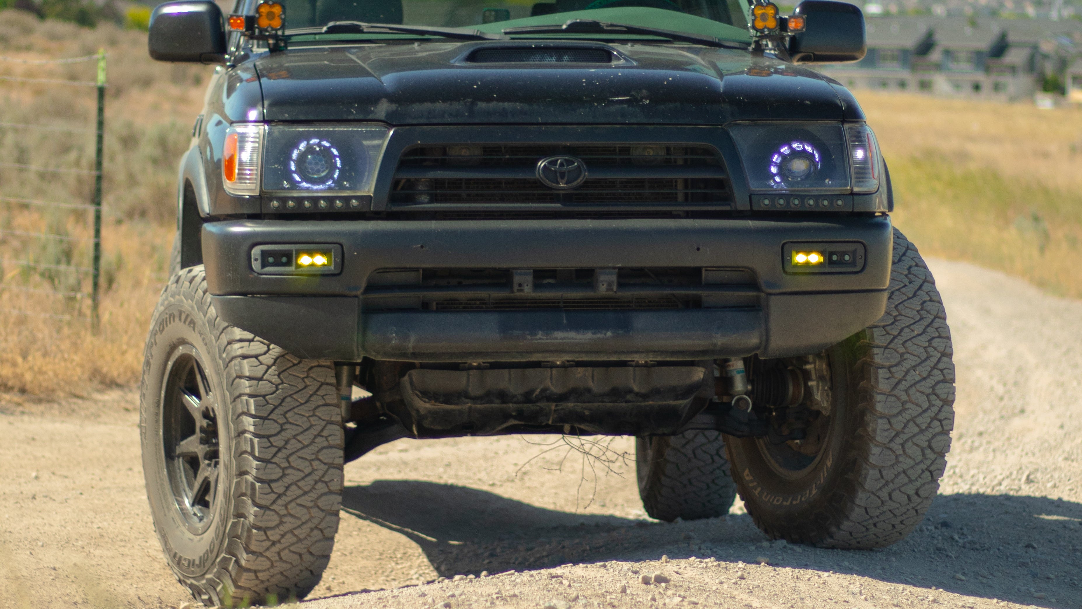 Black Toyota truck on a dirt road with mountains in the background with fog lights
